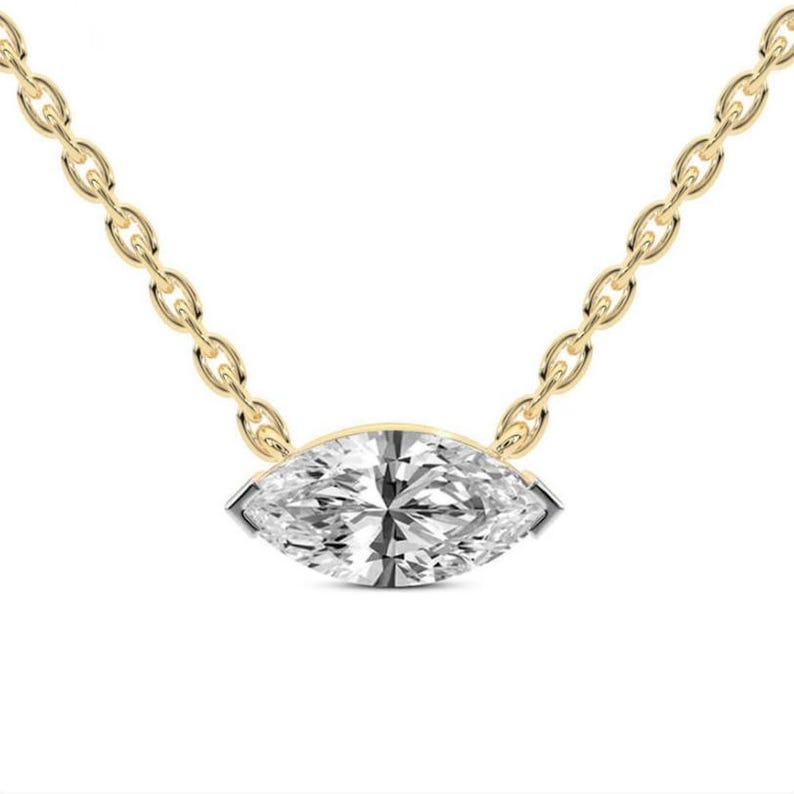 May include: A gold chain necklace featuring a marquise-cut diamond pendant. The diamond is set in a gold bezel and sparkles with many facets. The chain is delicate and has a classic link design.
