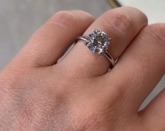 Op de afbeelding: Een zilveren verlovingsring met een grote, rond geslepen diamant. De diamant is gezet in een klassieke prongzetting en de band is dun en gepolijst. De ring wordt op een vinger getoond.