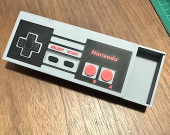 May include: A grey and black Nintendo controller with red buttons. The controller has a compartment on the back that can be opened.