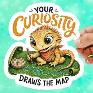 May include: A die-cut sticker featuring a yellow bearded dragon wearing a red bandana, holding a stick to draw on a large green leaf map. A compass sits on the leaf. The text reads YOUR CURIOSITY DRAWS THE MAP in black and orange lettering.