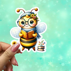 May include: A colorful sticker featuring a cartoon bee wearing glasses, a hat, and a scarf, holding a book. The bee is yellow and black with white wings. A small sunflower and a stack of books are also included in the design.