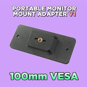 May include: A black rectangular portable monitor mount adapter V1 with a 100mm VESA pattern. The device features a central brass-coloured threaded insert and two side mounting holes, designed for secure attachment to a monitor stand or arm.
