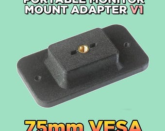 Pode incluir: Um adaptador de montagem para monitor portátil V1 preto de formato retangular com uma inserção roscada central na cor latão e dois orifícios de montagem laterais. O texto PORTABLE MONITOR MOUNT ADAPTER V1 e 75mm VESA aparece na imagem.