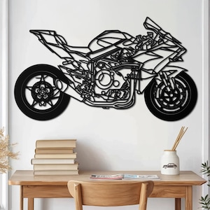 Op de afbeelding: Zwarte metalen motorfiets wandkunst. De motorfiets is afgebeeld in een gedetailleerde, geometrische stijl, met de motor, wielen en carrosserie. Het kunstwerk is gemonteerd op een witte muur, boven een houten bureau met boeken en een vaas.