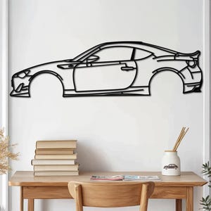 Peut inclure: Contour noir en métal d'une voiture de sport, vue de profil, sur un mur blanc. La voiture est un coupé avec un avant arrondi et un arrière légèrement incliné.