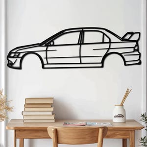May include: Black metal wall art of a car silhouette. The car is a side profile of a sports car with a spoiler. The art is mounted on a white wall above a wooden desk with books and a vase.