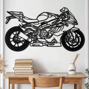 Könnte beinhalten: Schwarze Motorrad-Wandkunst aus Metall. Das Kunstwerk zeigt eine detaillierte Umrisszeichnung eines Sportmotorrads, einschließlich Rädern, Motor und Karosserie. Das Motorrad ist an einer weißen Wand über einem Holztisch befestigt.