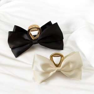 May include: Two large satin hair bows with gold metal clips. One bow is black and the other is ivory.