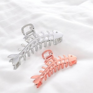 May include: Two hair clips shaped like fish skeletons. One is silver and the other is rose gold.