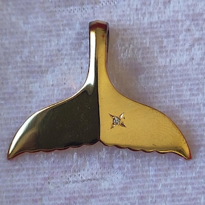 May include: Gold-tone whale tail pendant with a small clear rhinestone in the center.