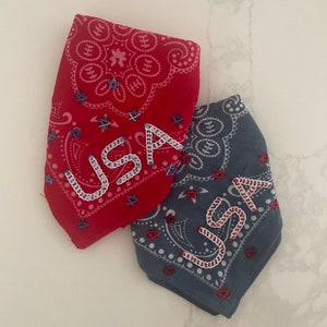 Puede incluir: Dos bandanas rojas, blancas y azules con la inscripci&oacute;n "USA" bordada. Las bandanas son de algod&oacute;n y tienen un patr&oacute;n paisley.