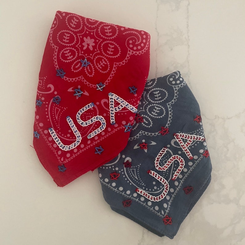 Puede incluir: Dos bandanas rojas, blancas y azules con la inscripci&oacute;n "USA" bordada. Las bandanas son de algod&oacute;n y tienen un patr&oacute;n paisley.