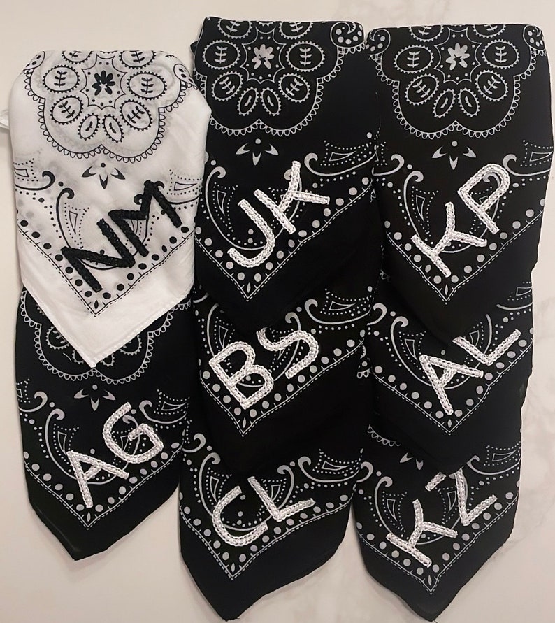 May include: Seven black bandana style fabric squares with white paisley designs and white embroidered letters. The letters spell out "AG, BS, CL, JK, KP, AL, KZ".