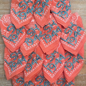 May include: A stack of orange bandanas with white paisley designs and blue embroidered text that reads "SKY 1944".
