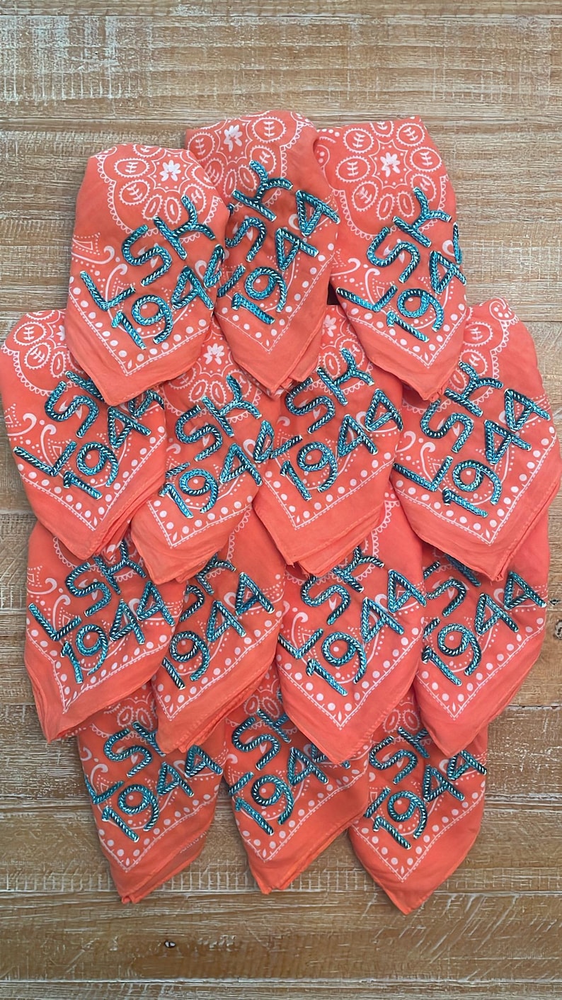 May include: A stack of orange bandanas with white paisley designs and blue embroidered text that reads "SKY 1944".