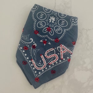 Puede incluir: Un pa&ntilde;uelo azul con un patr&oacute;n paisley blanco y estrellas rojas. La palabra "USA" est&aacute; bordada en blanco con puntadas rojas.