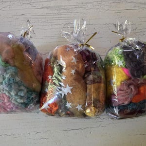 May include: Three clear cellophane bags filled with colorful fiber. The bags are tied with gold twist ties. The fiber inside is a mix of pink, blue, yellow, orange, and green. The middle bag has white star stickers.