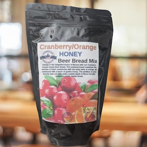 May include: A black bag of Cranberry/Orange Honey Beer Bread Mix. The bag features a photo of cranberries, oranges, and honey. The text on the bag reads "Cranberry/Orange Honey Beer Bread Mix".
