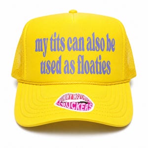 May include: A bright yellow trucker hat featuring a mesh back and a foam front panel. The text 'my tits can also be used as floaties' is printed in purple on the front. A pink lip-shaped sticker with the text 'FUNNY MOTHER TRUCKERS' is centered.
