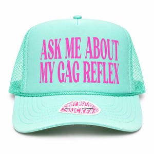 Könnte beinhalten: Eine mintgrüne Trucker-Cap mit Netzrücken und einem Schaumstoff-Frontpanel. Der Text ASK ME ABOUT MY GAG REFLEX ist in leuchtendem Pink auf der Vorderseite aufgedruckt. Ein kleiner Aufkleber mit dem Text FUNNY MOTHER TRUCKERS befindet sich auf dem Schirm.
