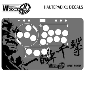 Op de afbeelding: Grijze Hautepad X1-stickers met witte knopcontouren en een Street Fighter-thema. Het ontwerp bevat een karakterillustratie, Japanse tekst en het Works-logo. Deze stickers zijn voor een gamecontroller.
