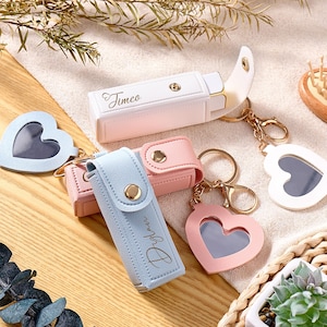 Può includere: Tre custodie rettangolari per rossetto con chiusure a scatto e portachiavi a forma di cuore. Una custodia bianca è incisa con il nome Timeo, una azzurra con il nome Dylan e una rosa è semplice. Tutte presentano finiture color oro.