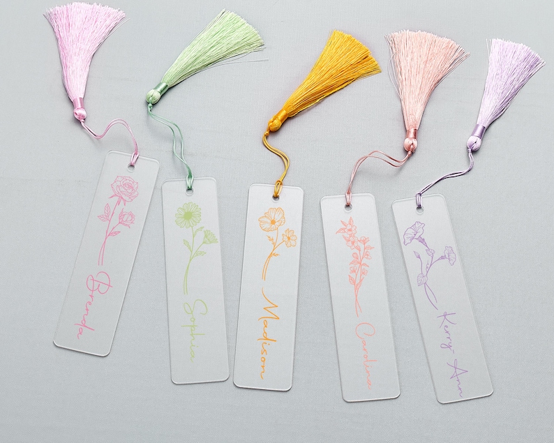 Op de afbeelding: Zes transparante acryl bladwijzers met kleurrijke kwastjes. Elke bladwijzer heeft een bloemenontwerp en een naam in bijpassende kleur: Brenda, Sophia, Madison, Caroline en Kerry Ann. De kwastjes zijn roze, groen, geel, perzik en paars.