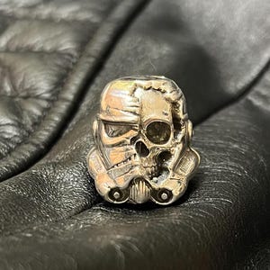 Op de afbeelding: Een zilveren ring met een gedetailleerd schedelontwerp, dat doet denken aan een Stormtrooper-helm uit Star Wars.