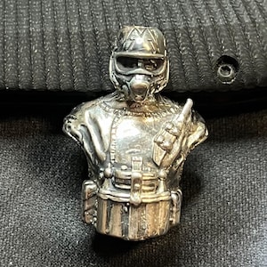 Op de afbeelding: Zilverkleurig beeldje van een futuristische soldaat, met een helm met bril, een ademhalingsmasker en een uniform met zakken. Het beeldje is zeer gedetailleerd en lijkt van metaal te zijn.