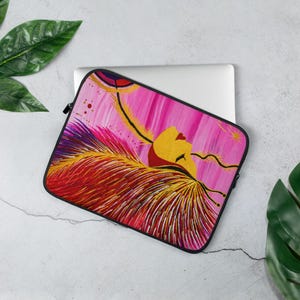 Könnte beinhalten: Laptop-Hülle mit abstraktem Gemälde in Rosa, Rot und Gelb. Das Design zeigt ein stilisiertes Gesicht und federartige Elemente. Die Hülle hat einen schwarzen Reißverschluss und eine schwarze Umrandung.