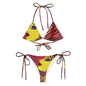 May include: A two-piece bikini set featuring a vibrant artistic design. The top is a triangle style with tie closures, and the bottom is a classic tie-side design. The artwork depicts a woman's face in yellow, red, and purple hues.