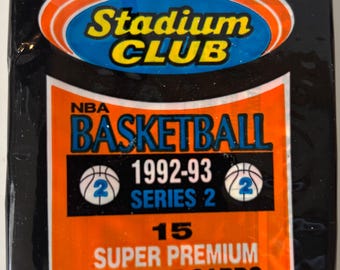 Può includere: Una confezione sigillata di figurine di basket NBA Topps Stadium Club 1992-93. L'involucro nero e arancione presenta il logo Topps Stadium Club, il testo 15 Super Premium Picture Cards e menziona la produzione con tecnologia ad alta definizione.