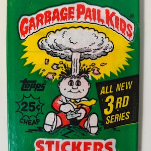 May include: A green Garbage Pail Kids sticker pack featuring a cartoon character with an explosion above its head. The pack includes the text "ALL NEW 3RD SERIES" and "STICKERS". The Topps logo and the price "25¢ CHEAP" are also visible.