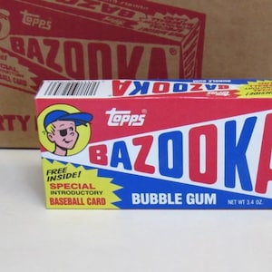 May include: A box of Bazooka bubble gum with a red, white, and blue design. The box features the word "BAZOOKA" in large letters and a cartoon character wearing a baseball cap. The box also states "Bubble Gum" and "Net Wt 3.4 oz."