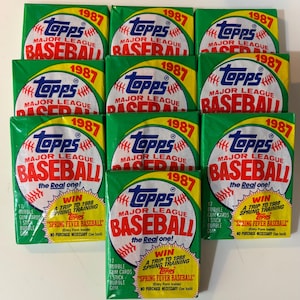 May include: A collection of eleven 1987 Topps Major League Baseball card packs. Each pack features a green background with a baseball graphic and the Topps logo. The packs include text that reads "Spring Fever Baseball".