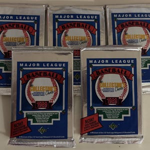 May include: Five silver foil packs of 1989 Major League Baseball Collector's Choice trading cards. Each pack features a blue and white design with the words "Major League Baseball" and "Collector's Choice" in a white banner. The packs are arranged in a row, with the front of each pack facing the viewer.