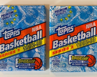 Può includere: Due pacchetti sigillati di figurine Topps NBA Basketball 1992-93, Serie 1 e Serie 2. Ogni involucro blu presenta motivi grafici bianchi, strisce diagonali arancioni e testo che indica 15 figurine e una carta Topps Gold in ogni pacchetto.