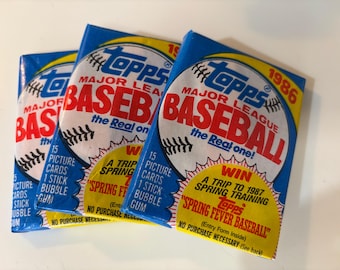 May include: Three packs of Topps Major League Baseball cards. The packs are blue and white with a baseball graphic and the text "Topps Major League Baseball the Real One!"  The packs are from 1986 and 1987.  The packs have a contest to win a trip to spring training.