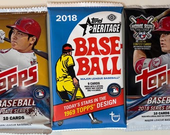 May include: Three Topps baseball card packs. The packs are labeled "2018 Update Series", "Heritage Baseball", and "2018 Series One". Each pack features a baseball player and the Topps logo. The packs contain 10 or 9 cards.