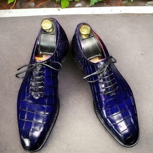 May include: A pair of blue leather dress shoes with a crocodile pattern. The shoes have lace-up closures and are pointed toe.