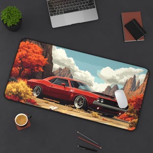 May include: A red vintage muscle car with a black interior is parked in a desert landscape with mountains in the background. The car is surrounded by trees and bushes. A white computer mouse is on the ground in front of the car.