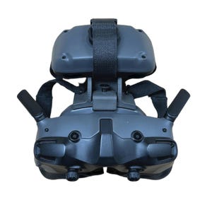May include: A dark gray virtual reality headset with a black strap and two antennas. The headset has a textured surface and two lenses. The design includes adjustable straps for a secure fit. The device is designed for immersive gaming and virtual experiences.