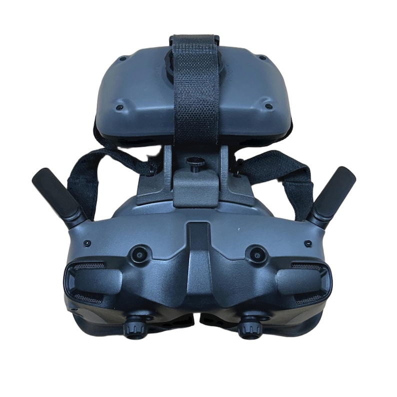 May include: A dark gray virtual reality headset with a black strap and two antennas. The headset has a textured surface and two lenses. The design includes adjustable straps for a secure fit. The device is designed for immersive gaming and virtual experiences.