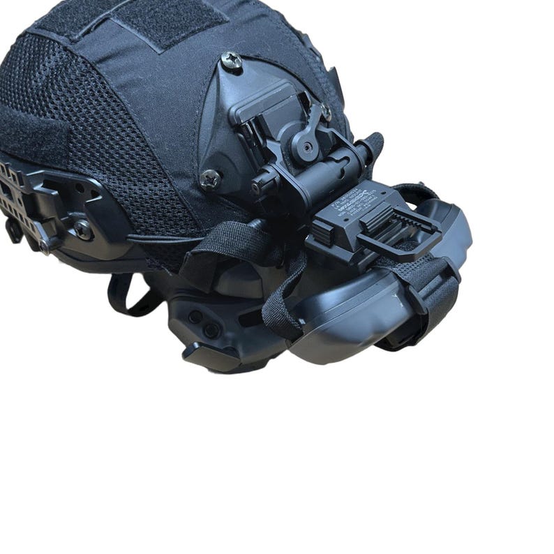 May include: Black tactical helmet with attached night vision equipment. The helmet features a mesh fabric cover and various mounting brackets. Straps and adjustment components are visible, along with a clear, white background.
