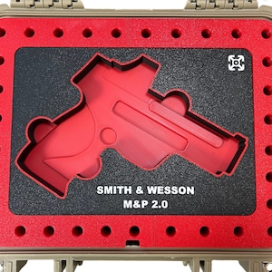 May include: A tan hard case with a red interior. The interior has a cutout for a handgun, with the text "SMITH & WESSON M&P 2.0". The case is designed to protect the contents.