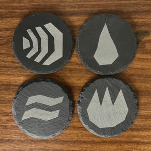 May include: Four black slate coasters with different white symbols. The symbols are a wave, a flame, a drop of water, and a geometric shape.