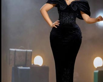 Könnte beinhalten: Ein schwarzes Samt-Abendkleid mit schulterfreien Ärmeln und einem figurbetonten Oberteil. Das Kleid hat eine glitzernde Pailletten-Taille und einen bodenlangen Rock. Das Model trägt Schmuck und hat die Haare hochgesteckt.