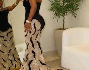 Könnte beinhalten: Ein schwarzes und beiges Abendkleid mit Meerjungfrau-Silhouette. Das Oberteil ist schwarz, während der Rock eine beige Spitzenauflage mit schwarzen, geschwungenen Verzierungen aufweist. Das Kleid hat eine lange Schleppe und wird mit Schmuck getragen.