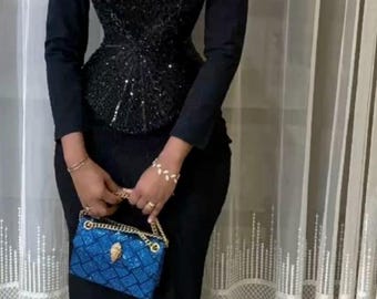 Könnte beinhalten: Ein formelles schwarzes Kleid-Ensemble. Das Outfit umfasst einen langen schwarzen Rock, ein figurbetontes Oberteil mit Pailletten-Oberteil und eine passende langärmlige Jacke. Eine kleine blaue Handtasche mit goldenem Kettenriemen vervollständigt den Look.