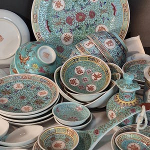 May include: A collection of antique porcelain dishware with a teal and white floral design. The set includes plates, bowls, and serving spoons. The dishes have red and gold accents and Chinese characters.